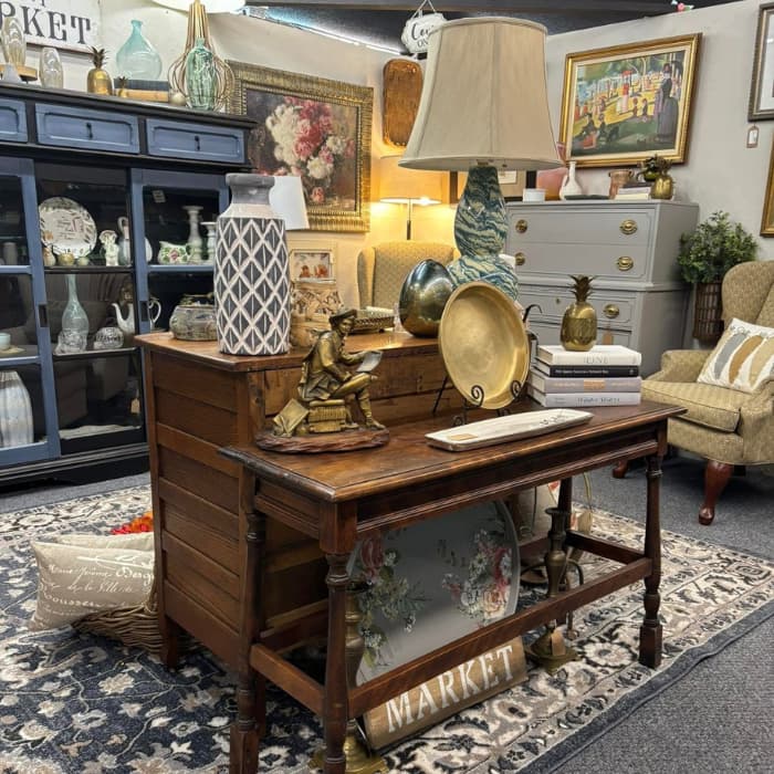 Curated vintage home decor setup with a wooden desk, gold accents, vases, a reading figurine, and layered art in a cozy booth setting.