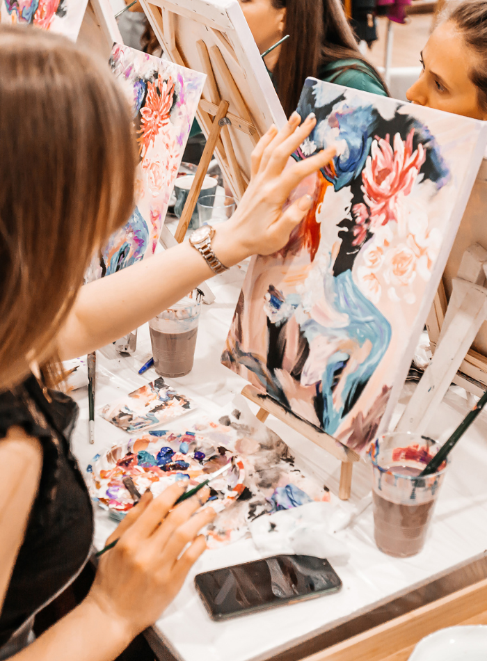 Woman painting a colorful abstract floral canvas during an art class.