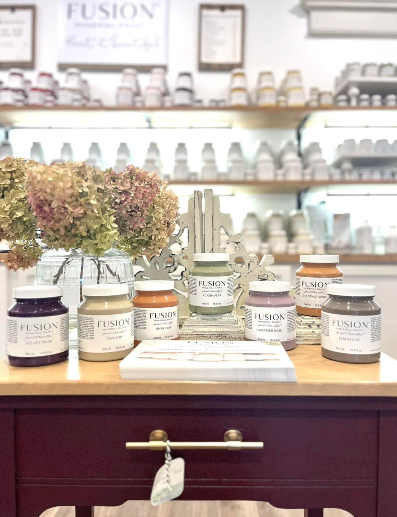 Curated vintage home decor setup with a wooden desk, gold accents, vases, a reading figurine, and layered art in a cozy booth setting.