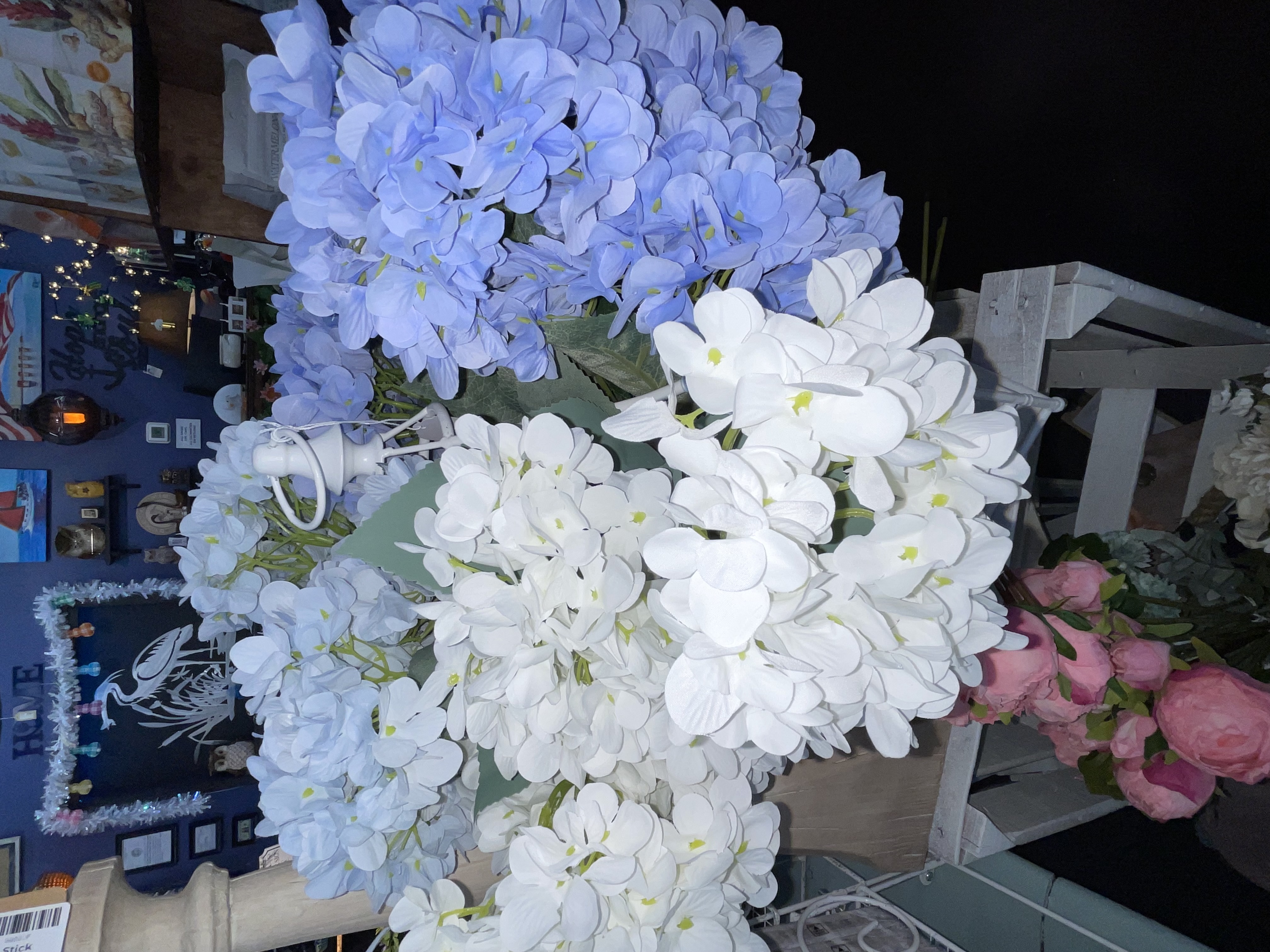 Boutique clothing display with a floral puff-sleeve blouse, white pants, canvas beach totes, and racks of colorful summer outfits.