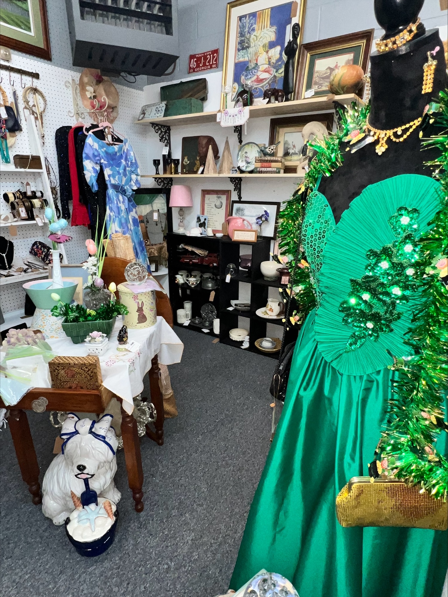 Boutique clothing display with a floral puff-sleeve blouse, white pants, canvas beach totes, and racks of colorful summer outfits.