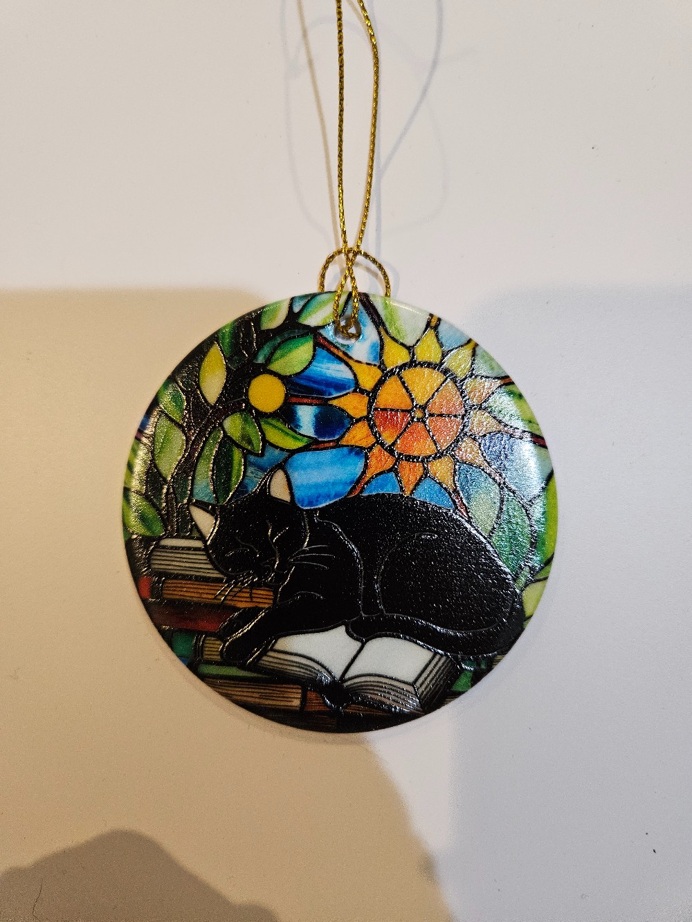 a black cat sleeping on a stack of books ornament with a colorful stained-glass style backdrop.