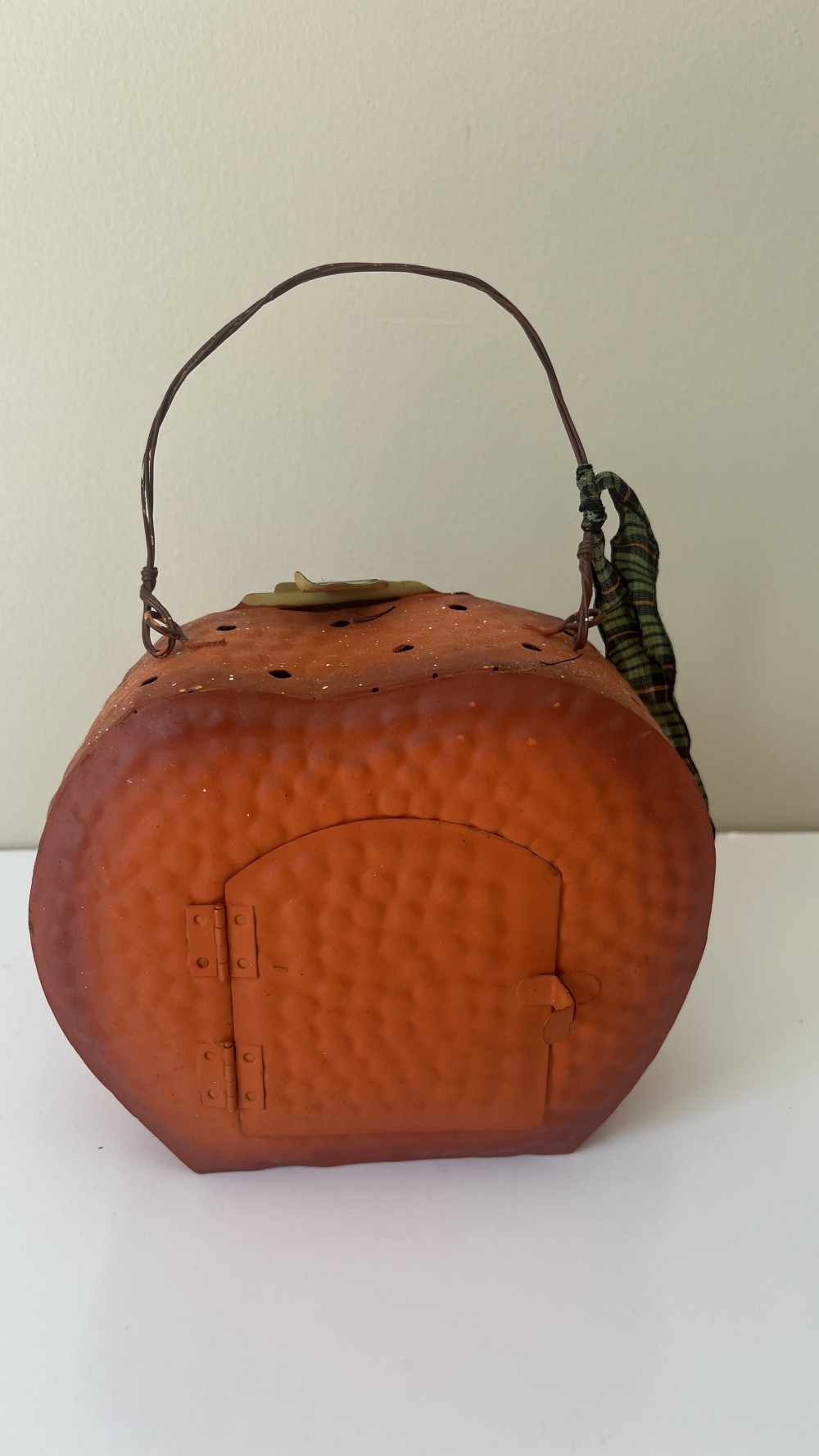 Vintage-style metal jack-o'-lantern pumpkin container with a wire handle and a plaid ribbon.