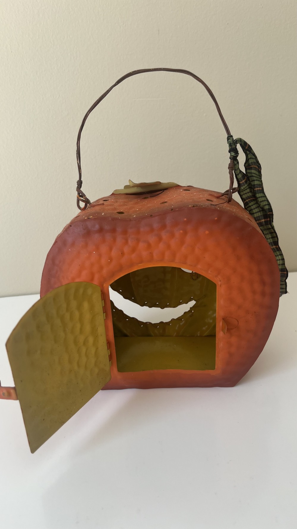Vintage-style metal jack-o'-lantern pumpkin container with a wire handle and a plaid ribbon.