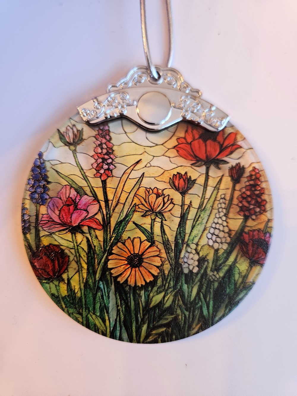 This wildflower suncatcher features a vibrant, printed floral design encased in a circular frame