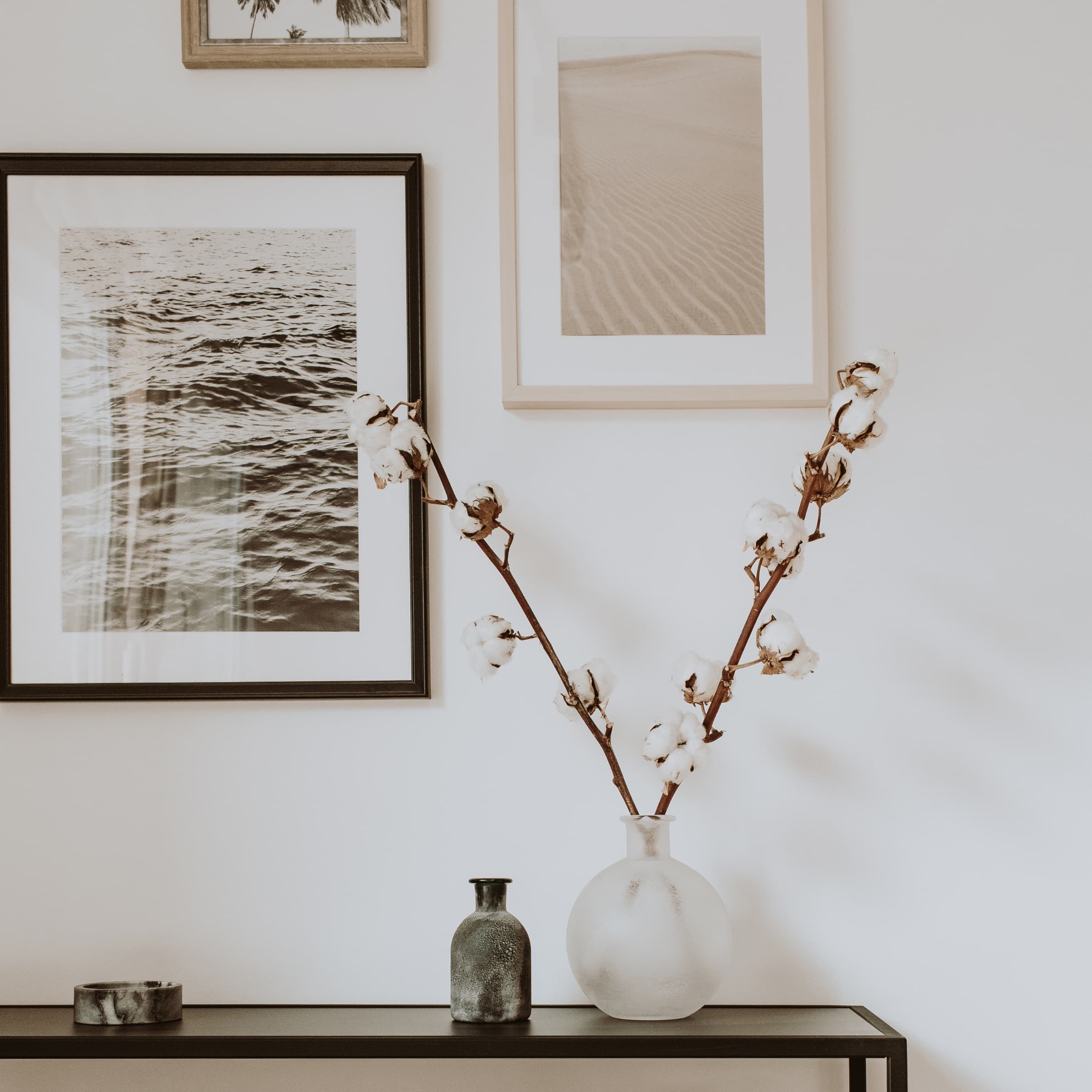 Upclose photo of a stand with cotton decor sticking out of a vase and scenery photos hanging on the wall.