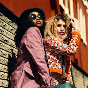 Two women standing side by side outdoors posing for a photo in bright colored clothes.