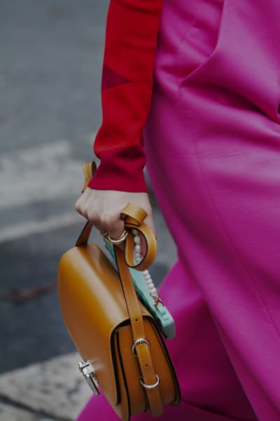 A close up photo of a women walking on the street in a pink blazer holding a brown leather bag.