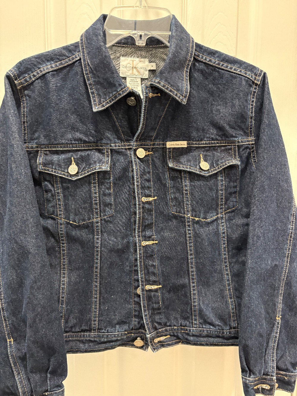 A Calvin Klein, jean jacket with a scrappy American flag on the back in a size medium