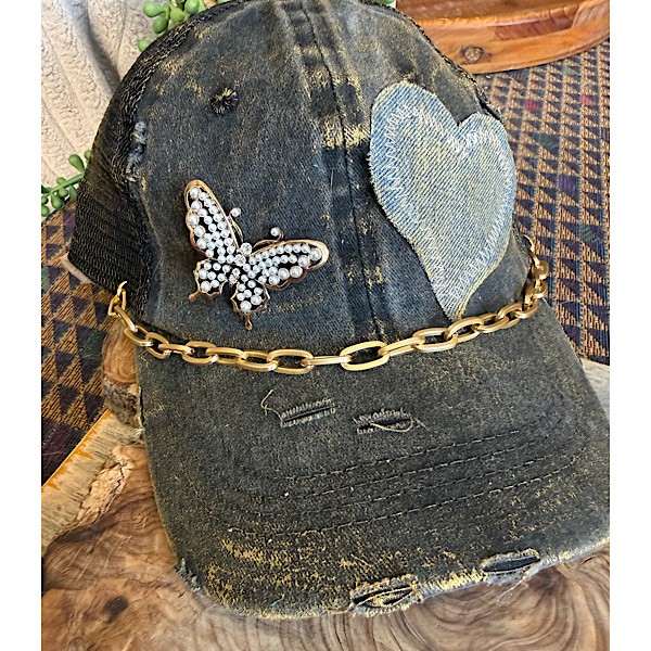 Hat: Gold brushed charcoal distressed tucker hat w/denim heart applique, pearled butterfly brooch and gold chain accent and vintage brooch